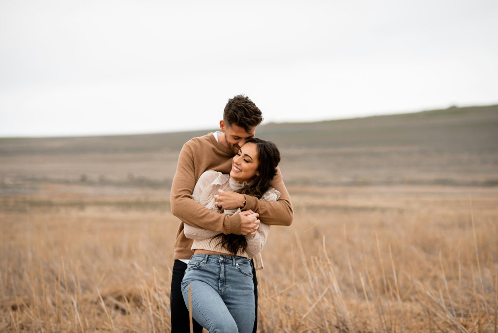 a man and woman wearing engagement ring hugging in a field 